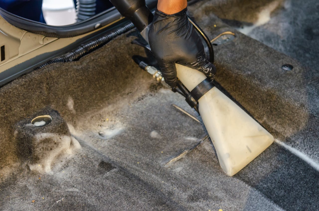 Mastering the First Impression: Your intriguing post title goes here A hand in a glove using a vacuum to clean a car interior carpet, removing dirt effectively.